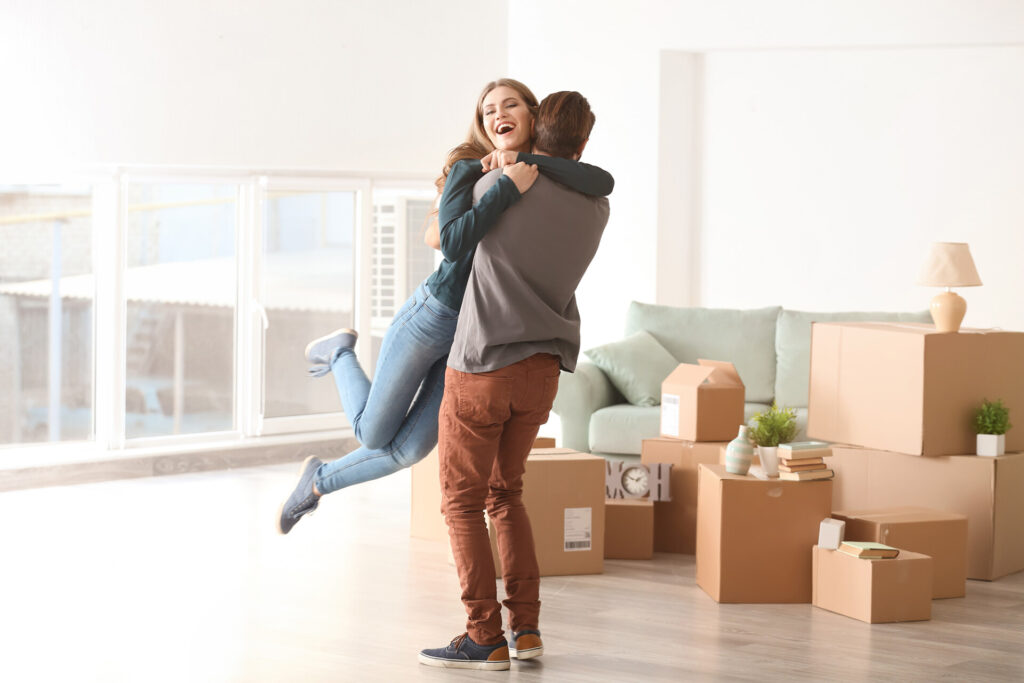 Young Happy Couple In Room With Moving Boxes At New Home