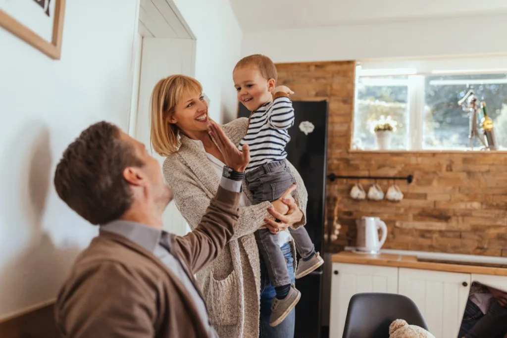 Mama in oče z otrokom starim 2 leti v naročju, oče daje petko sinu